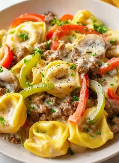 A bowl of Crock Pot cheesesteak tortellini topped with cheese and herbs.