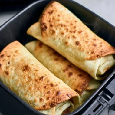 Golden brown chimichangas cooked in an air fryer topped with guacamole and salsa.