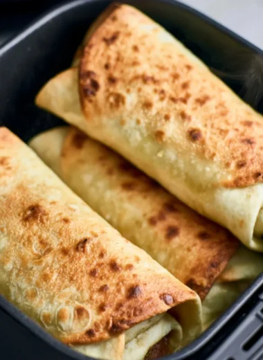 Golden brown chimichangas cooked in an air fryer topped with guacamole and salsa.