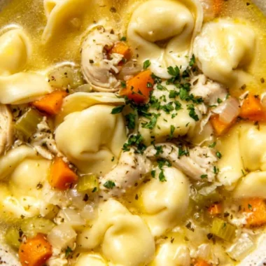 A bowl of delicious Chicken Tortellini soup garnished with herbs and vegetables.