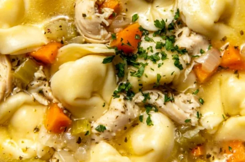 A bowl of delicious Chicken Tortellini soup garnished with herbs and vegetables.