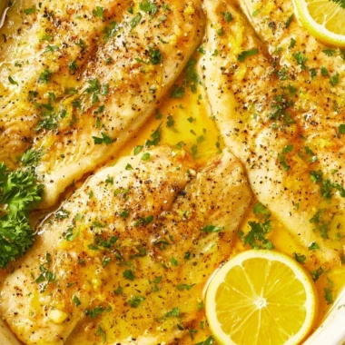 Oven baked tilapia served with lemon and herbs on a plate.