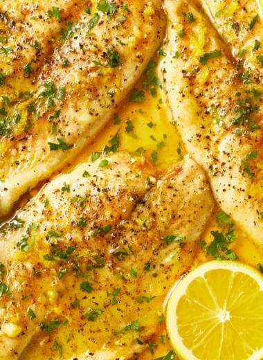 Oven baked tilapia served with lemon and herbs on a plate.